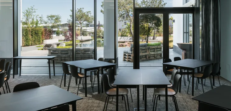 Modern conference room with black group tables and wooden chairs, offering a view of the garden through large glass windows.