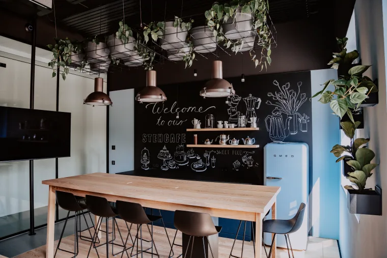 A modern meeting room with a wooden table, whiteboard, hanging plants and stylish pendant lights creating a welcoming atmosphere.