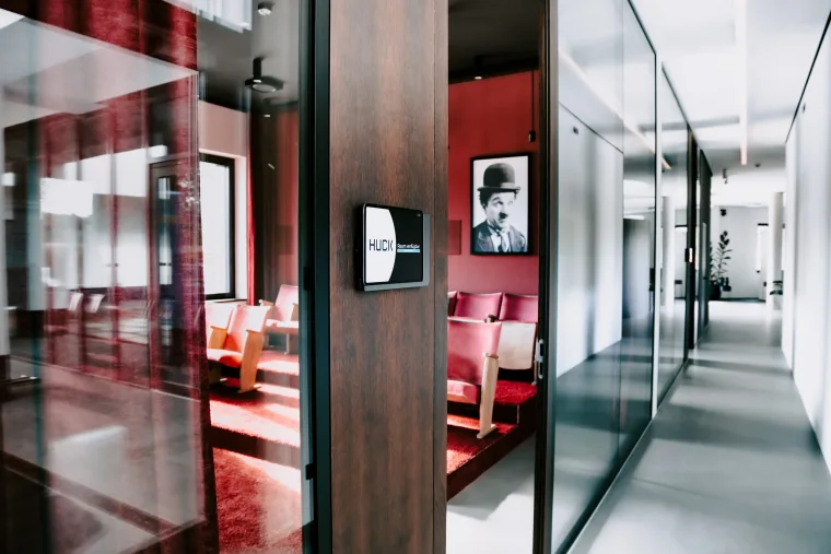 Modern office interior with a glass door holding a tablet, a red cinema room on the left and a bright hallway.