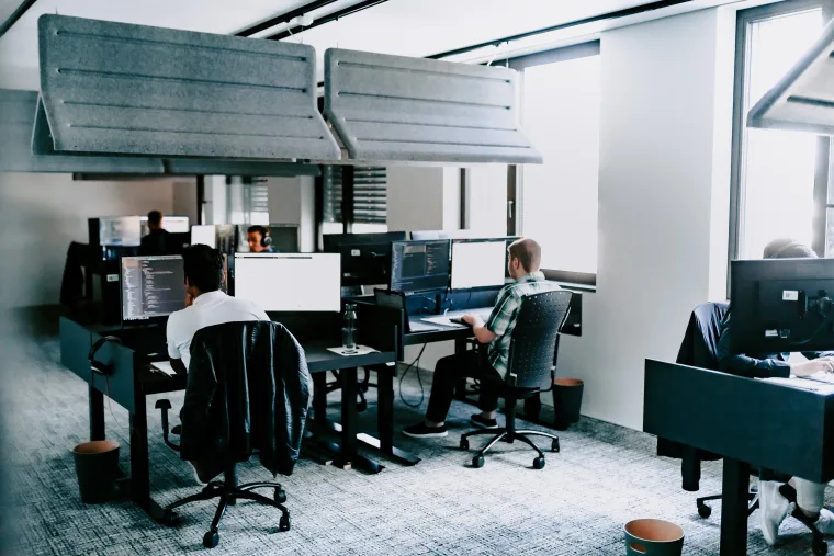 Three people working at desks in a modern office, focused on their computer screens, with sound-insulating panels mounted above.