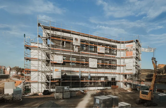 A construction site with a scaffolded building bearing signs, surrounded by machinery and stacked materials.